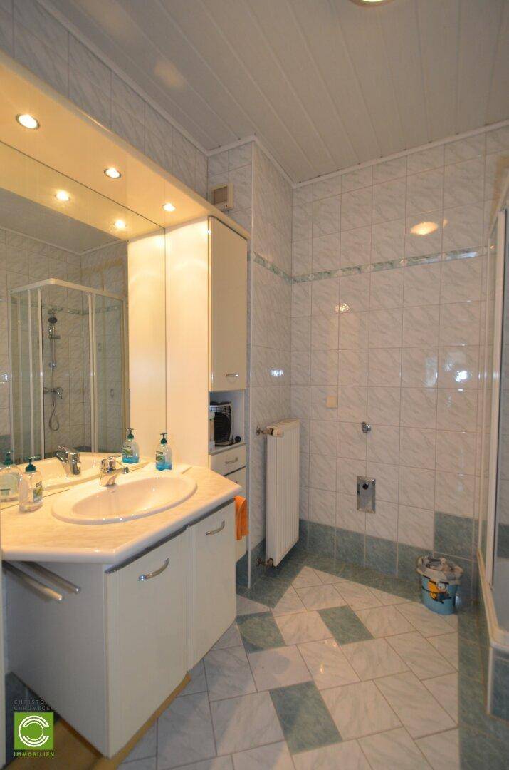 Badezimmer mit hellblauen und weißen Fliesen, Einzelwaschbecken und Spiegelschrank.
