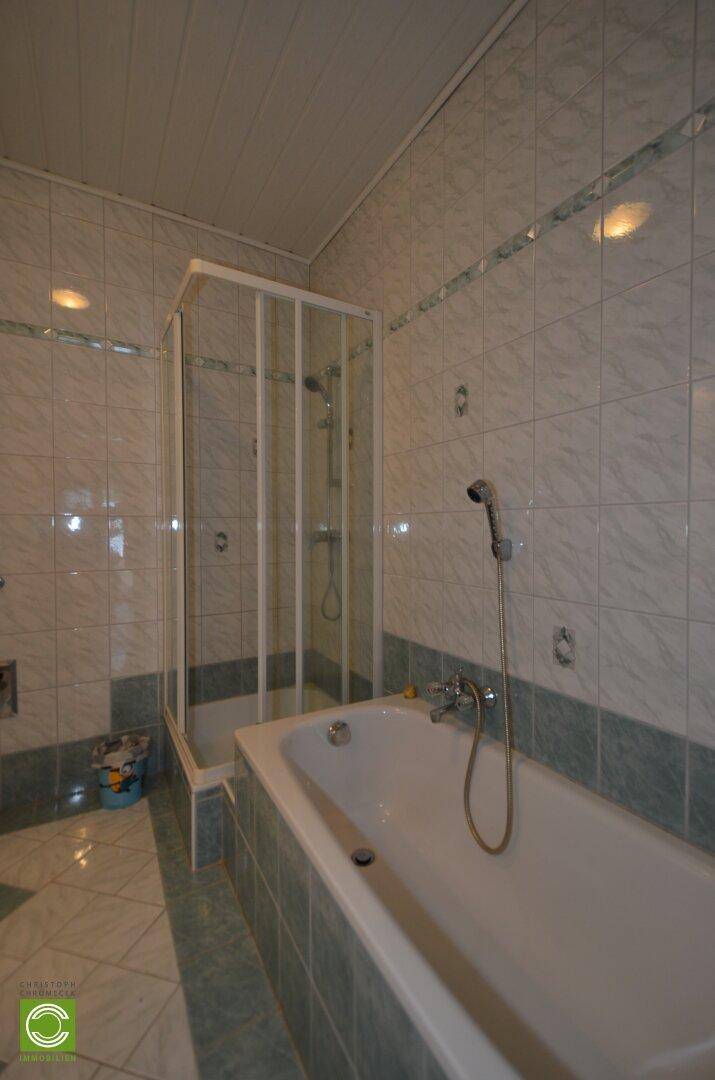 Gefliestes Badezimmer mit Duschkabine und Badewanne, ausgestattet mit einem Heizkörper.