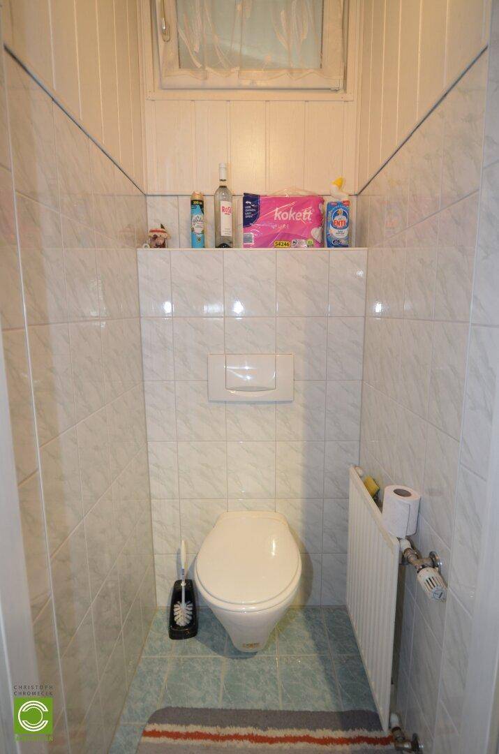 Kleines Gäste-WC mit Wand-WC, Fliesen und einem kleinen Fenster für Belüftung.