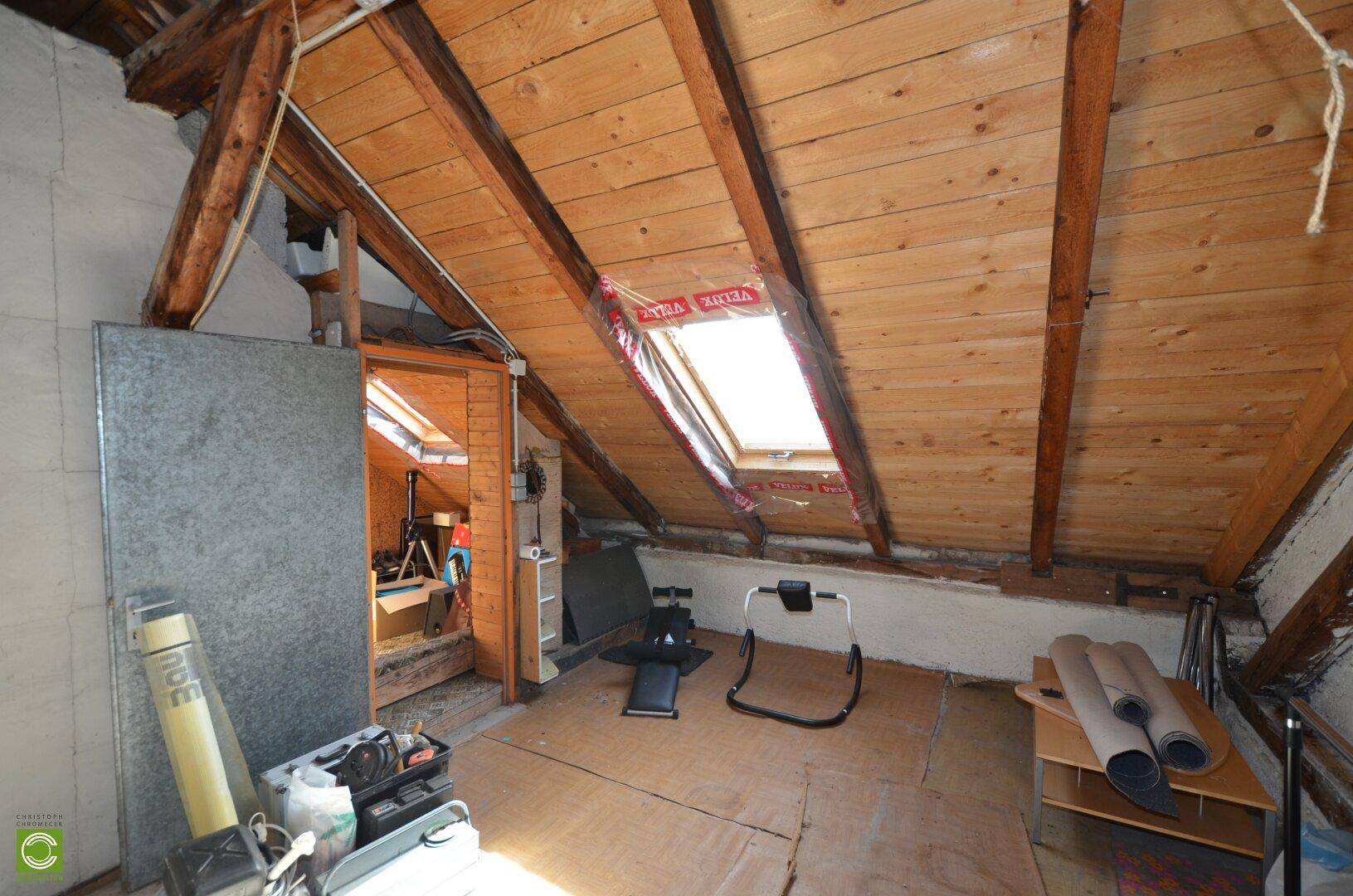 Dachboden mit sichtbaren Holzbalken, Dachschrägen und einem Dachfenster für natürliches Licht.