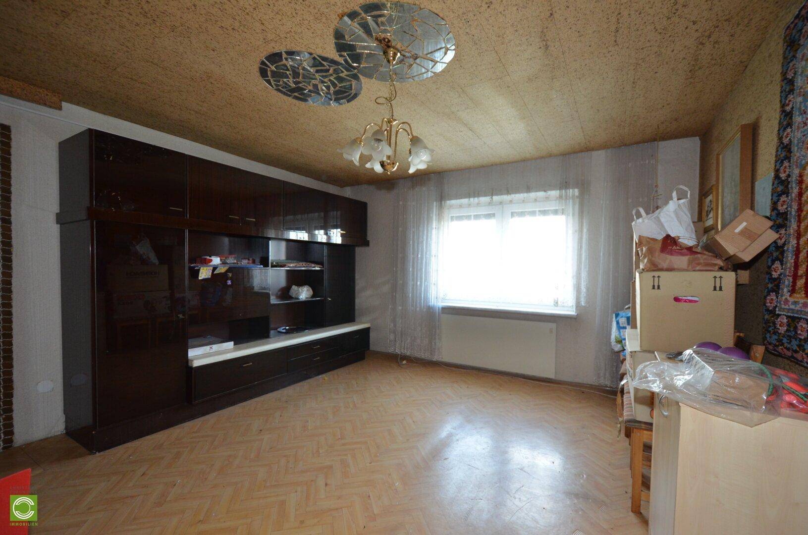 Wohnzimmer mit dunklem Wandschrank, gemusterter Decke und einem Fenster mit Vorhängen.