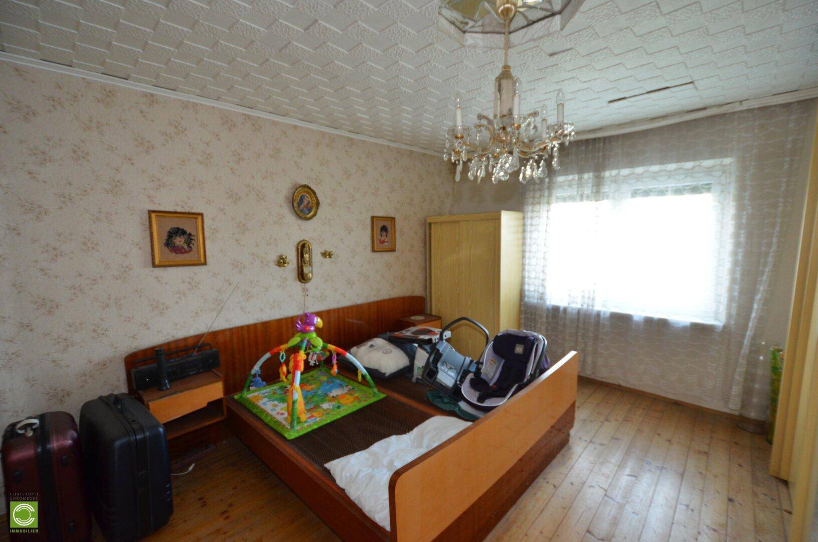 Schlafzimmer mit Holzbett, gemusterter Tapete und einem großen Fenster, das den Raum erhellt.