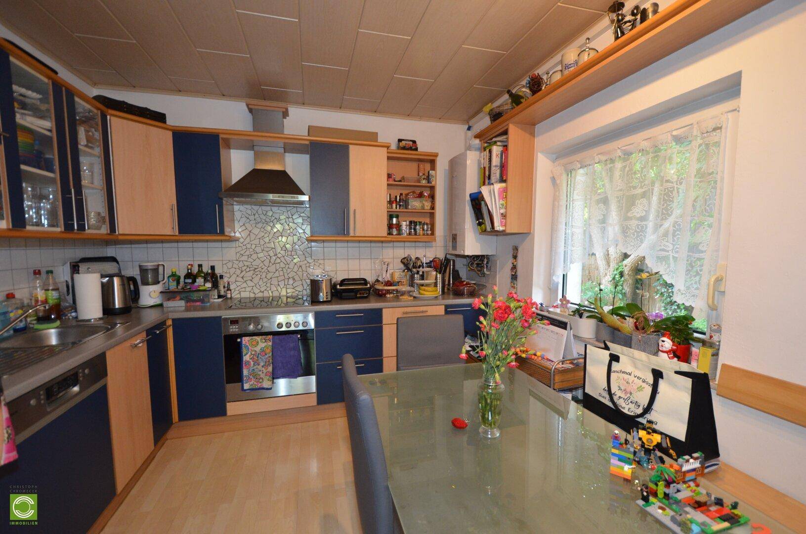 Geräumige Küche mit blauen und holzfarbenen Schränken, Essbereich und Fenster zum Garten.