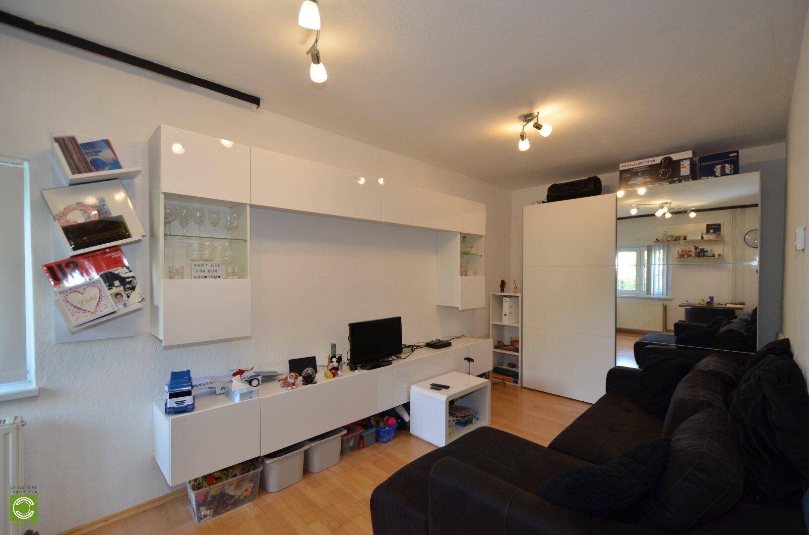 Helles Wohnzimmer mit modernem weißen Mediamöbel, dunklem Sofa und Parkettboden.