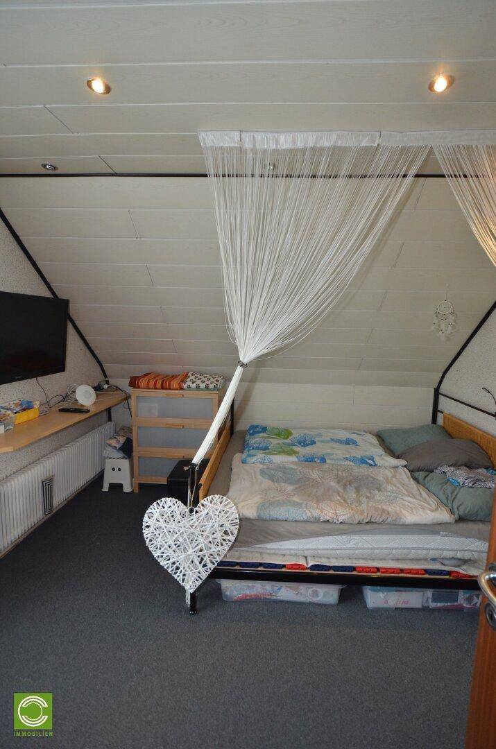 Gemütliches Schlafzimmer im Dachgeschoss mit schrägen Wänden, Teppichboden und Himmelbett.