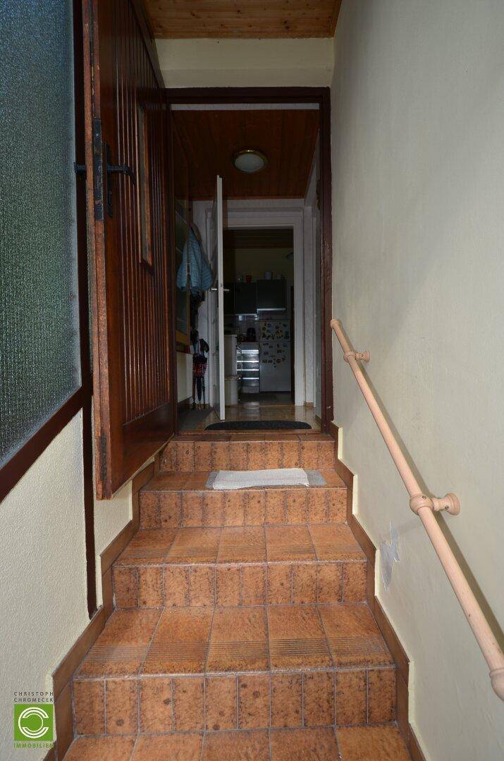 Eingangsbereich mit gefliesten Stufen, Holzvertäfelung und Zugang zu weiteren Räumen.