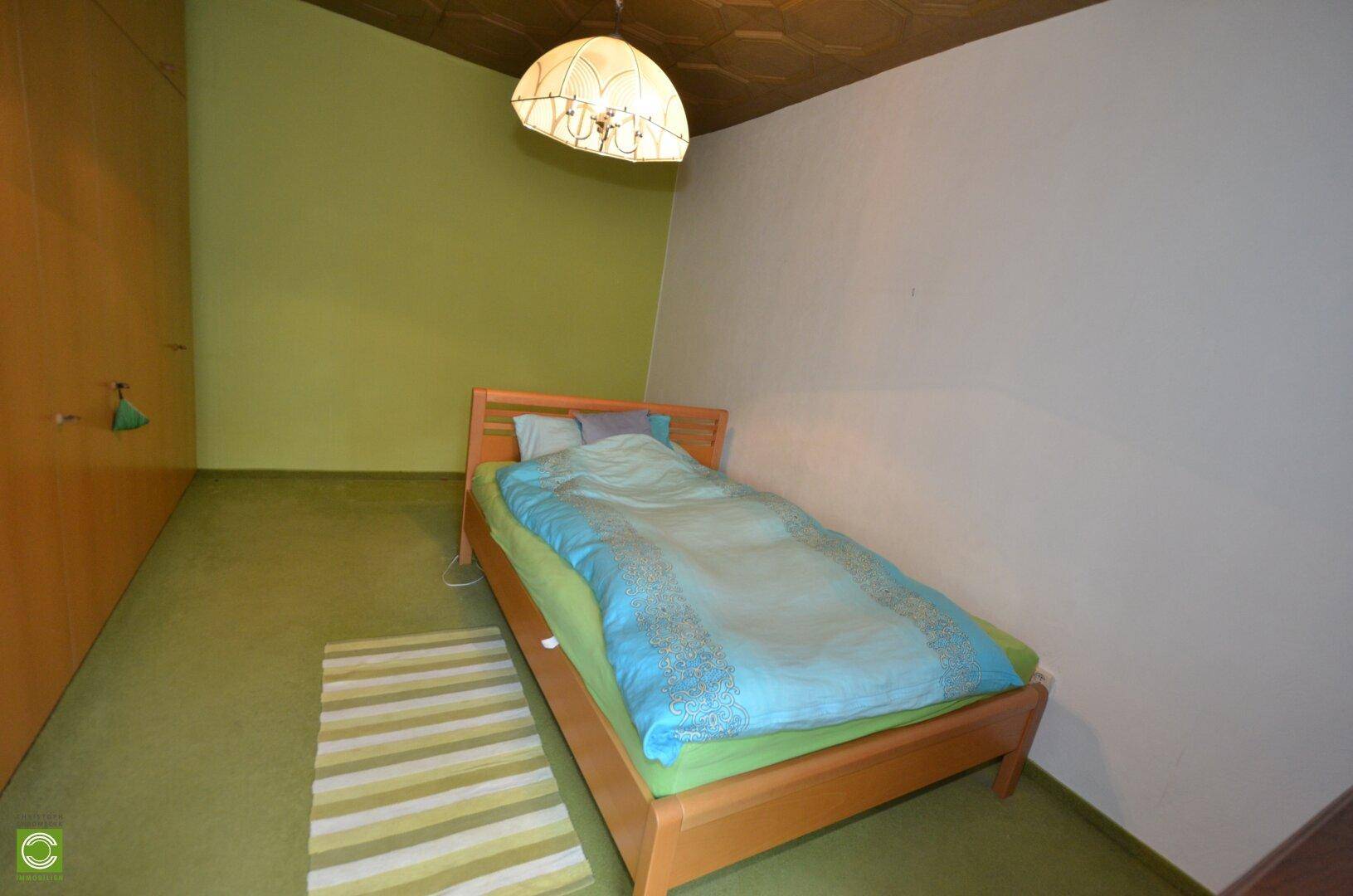 Schlafzimmer mit grünem Teppichboden, Holzbett und schrägen Wänden im Dachgeschoss.