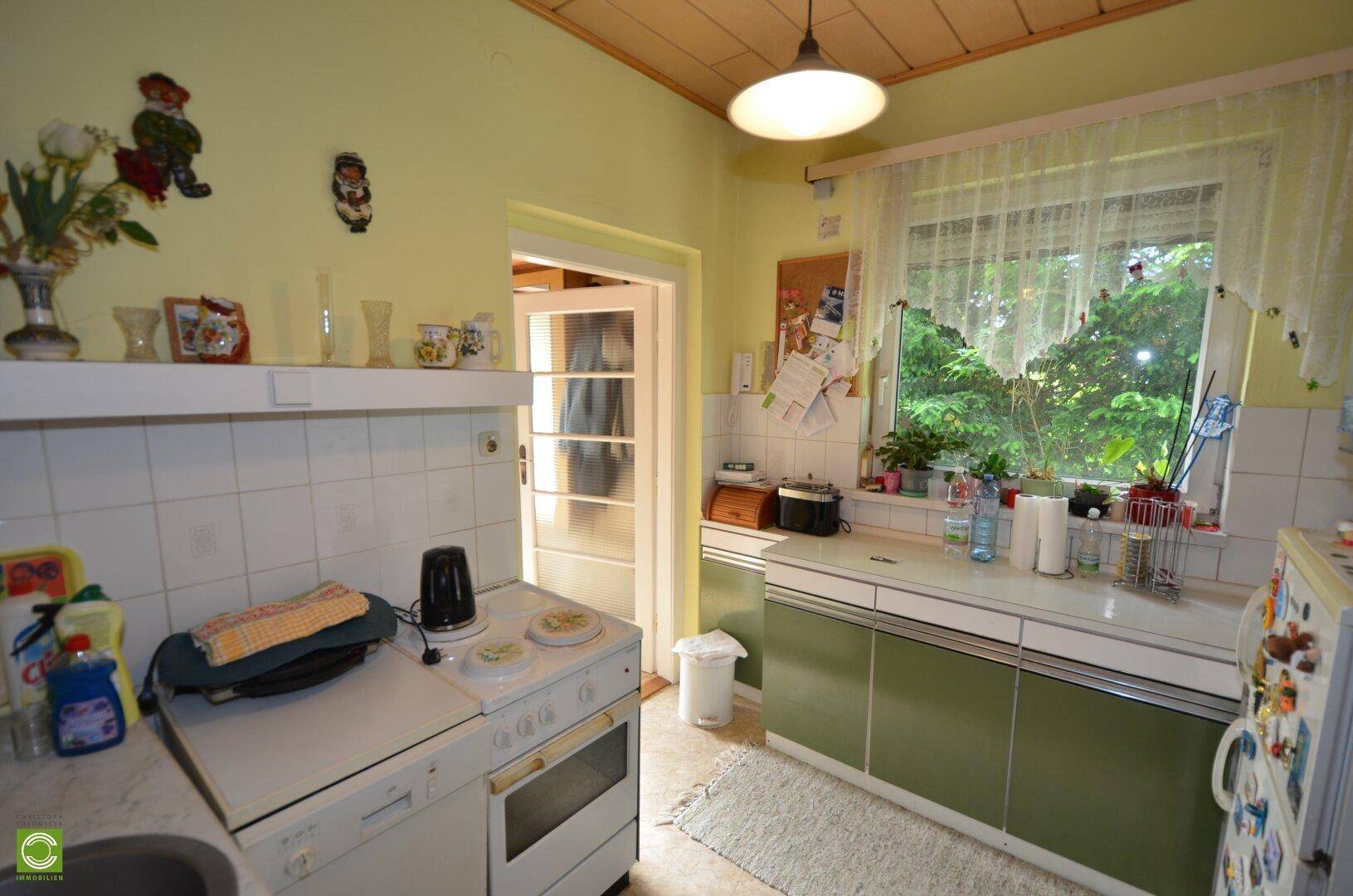 Helle Küche mit grünen Unterschränken, weiß gefliestem Bereich und Fenster zum Garten.