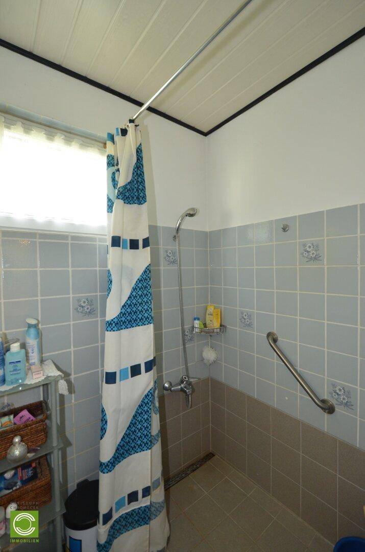 Badezimmer mit Dusche, hellblauen Fliesen und Haltegriff für mehr Sicherheit.