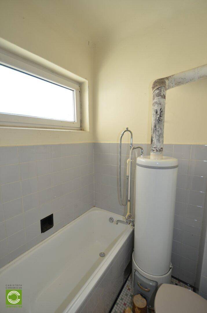 Badezimmer mit Badewanne, WC und Boiler, hell gefliest und mit kleinem Fenster.