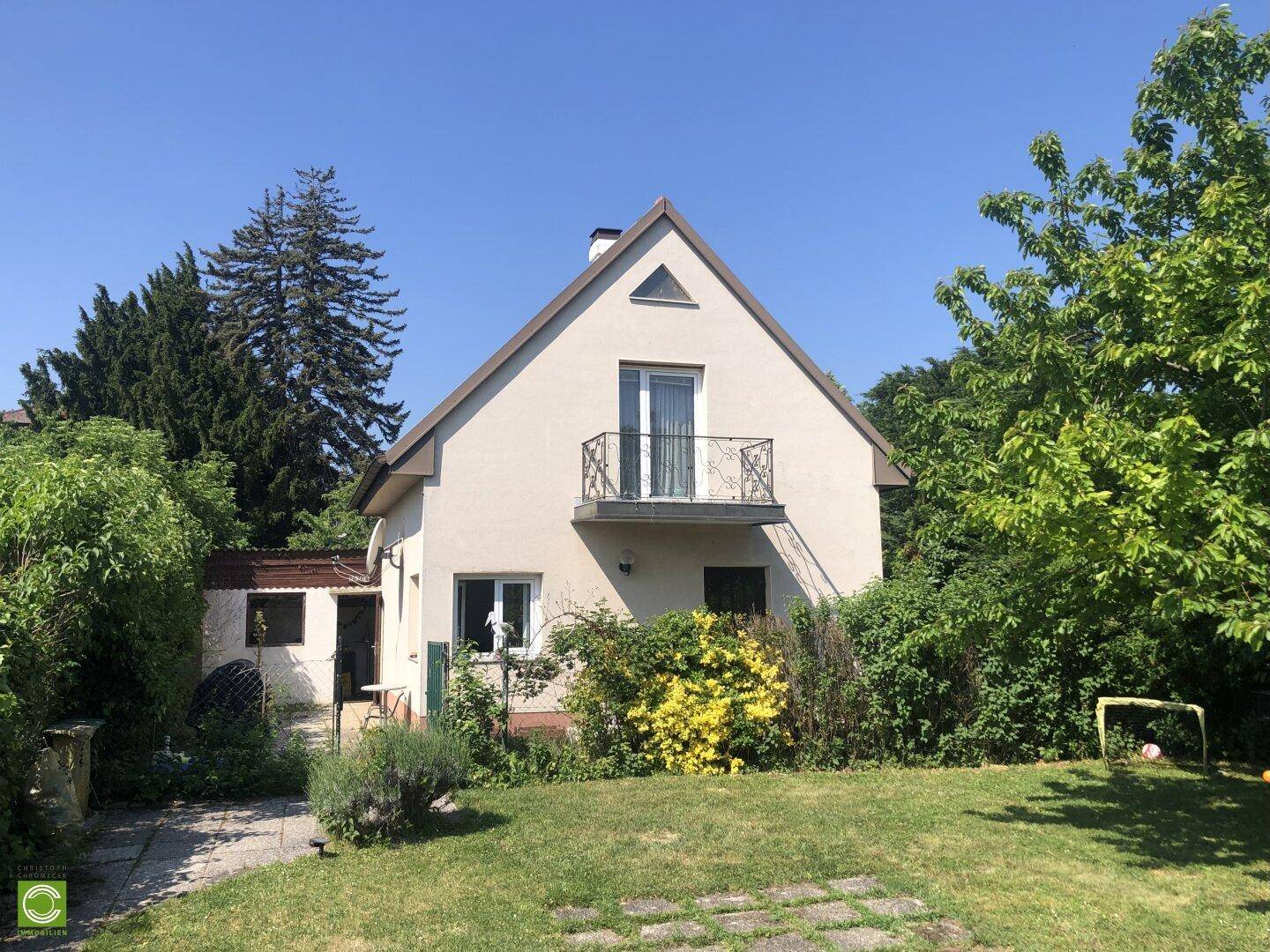 Vorderansicht des Hauses mit Garten, Rasenfläche und einem kleinen Balkon im Obergeschoss.