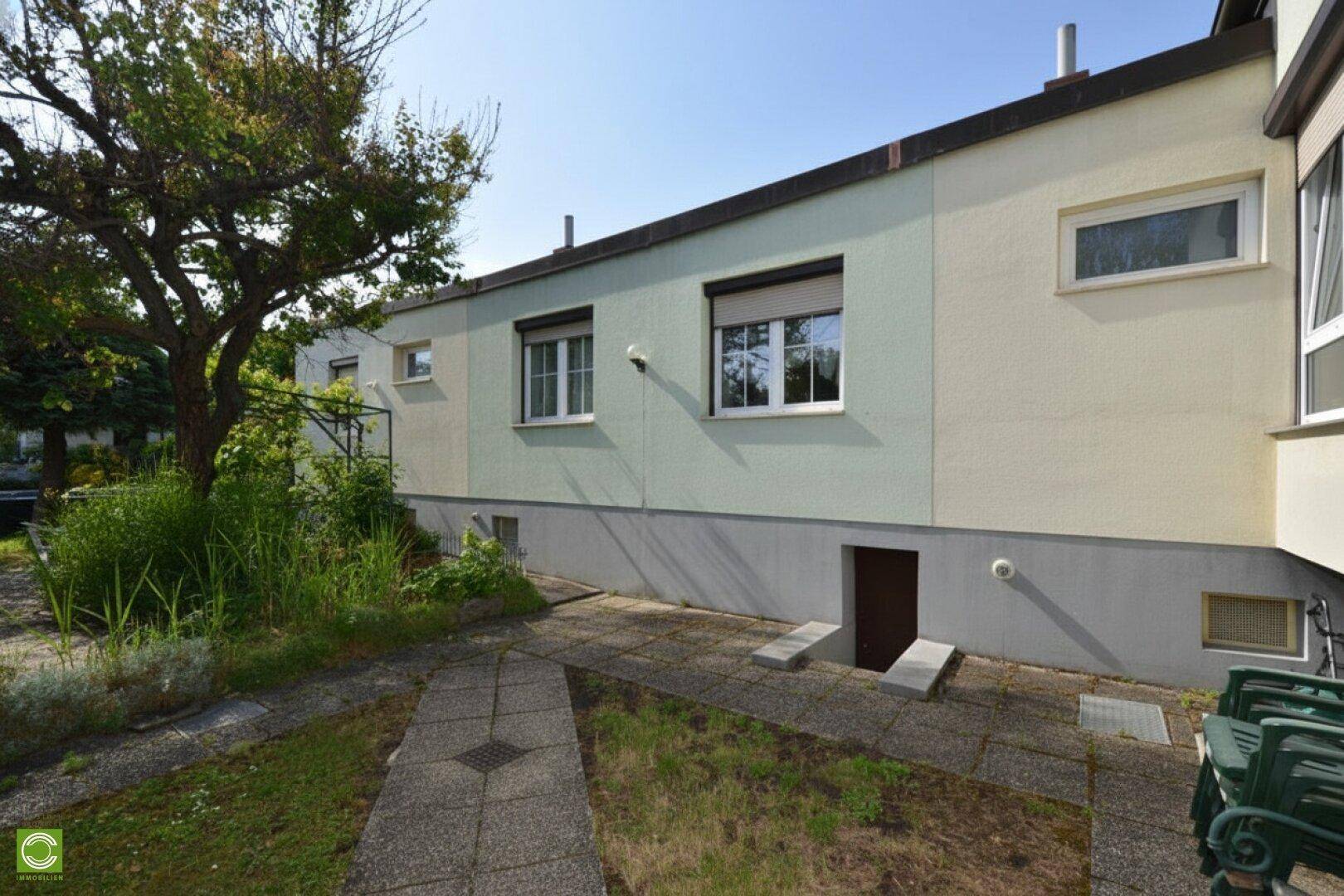 Rückseite des Hauses mit Gartenbereich, gepflastertem Weg und Zugang zum Keller.
