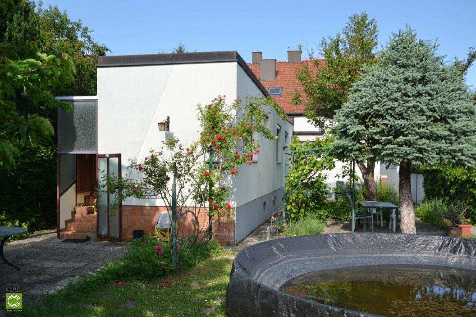 Gartenbereich mit kleinem Teich, Sitzgelegenheiten und blühenden Rosensträuchern vor dem Haus.