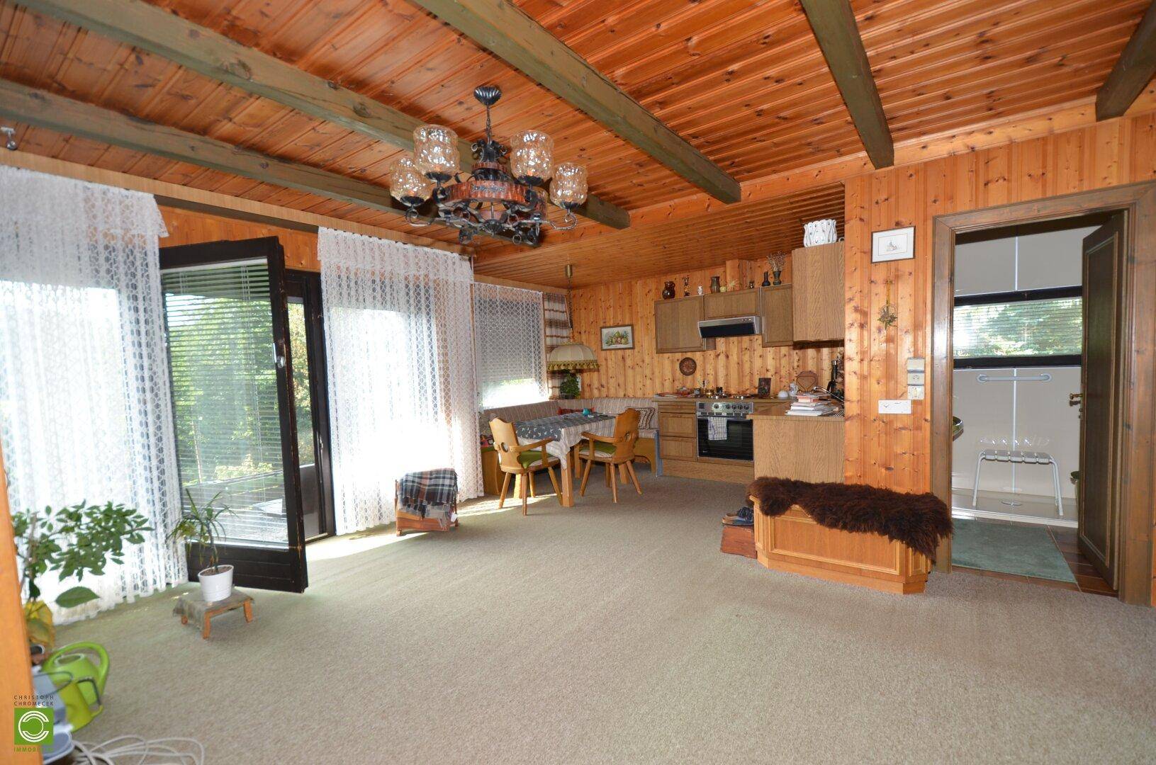Rustikaler Wohn- und Essbereich mit offener Küche, Holzwänden und sichtbaren Deckenbalken.