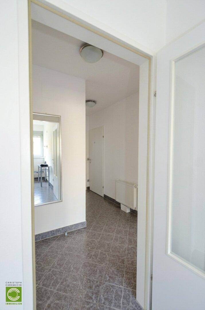 Eingangsbereich mit Fliesenboden, weiß gestrichenen Wänden und einem Wandspiegel.