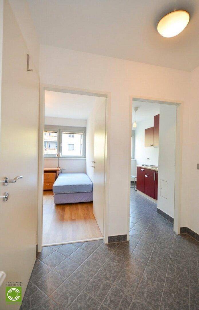 Flur mit Fliesenboden und Zugängen zu einem Schlafzimmer und einer kleinen Küchenzeile.
