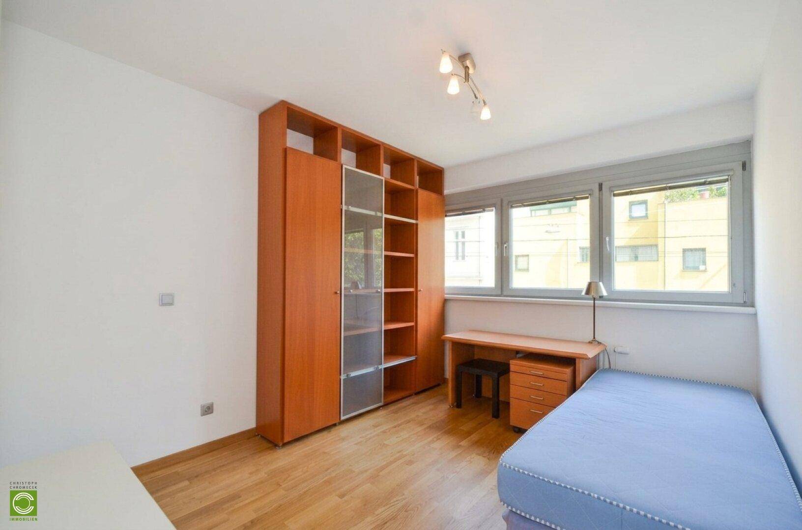Helles Schlafzimmer mit Holzfußboden, Einzelbett, Schreibtisch und großem Holzregal.