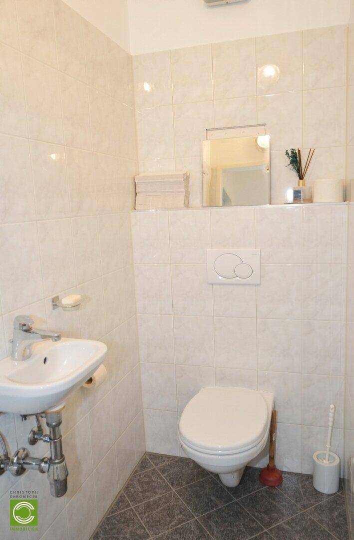Gäste-WC mit weißen Fliesen, wandhängendem WC und kleinem Handwaschbecken.