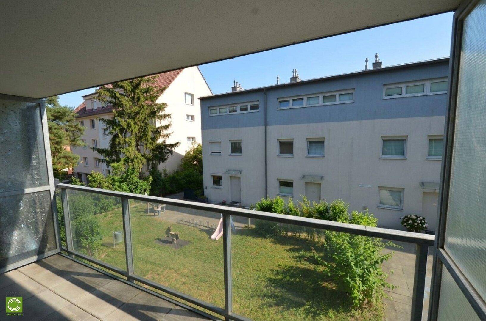 Balkon mit Fliesenboden und Blick auf den gemeinschaftlichen Gartenbereich mit Spielplatz.