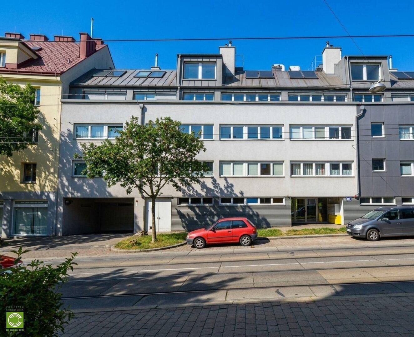 Mehrstöckiges Wohngebäude mit moderner Fassade und geparkten Autos an der Straße.