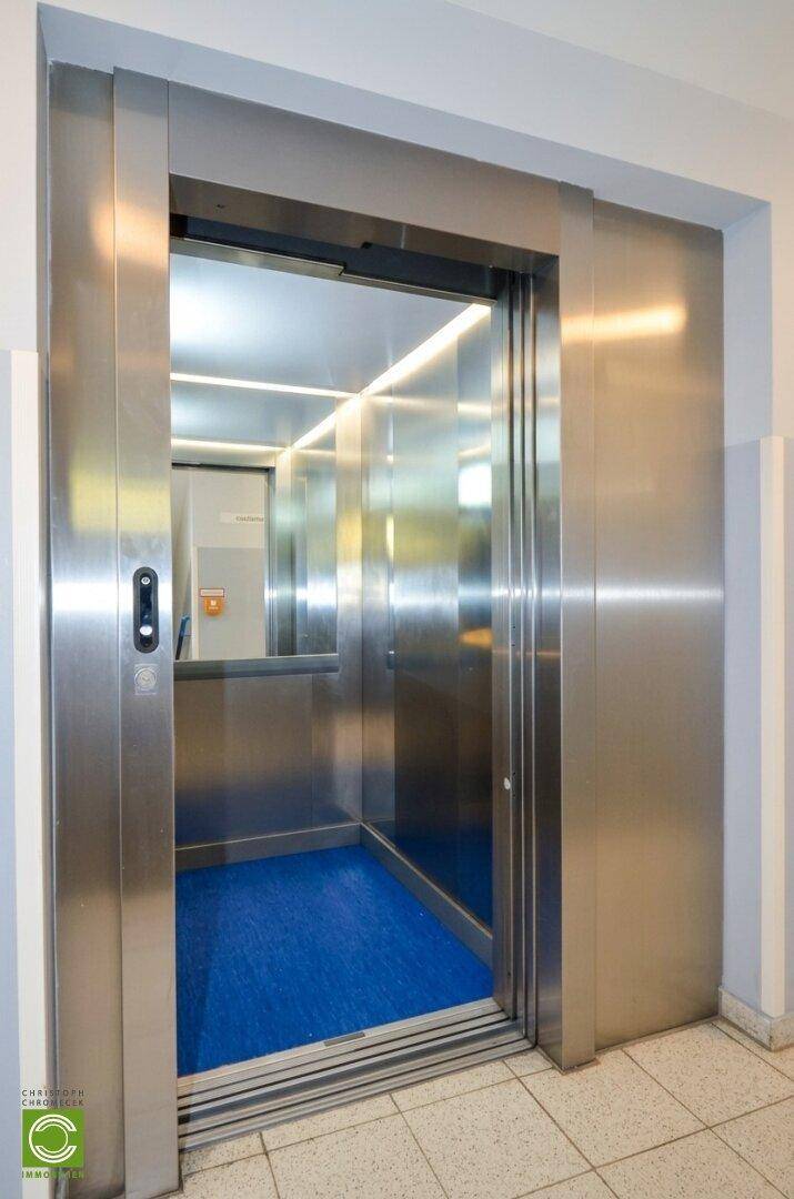 Moderner Aufzug mit Edelstahltüren und einem blauen Bodenbelag im Inneren.