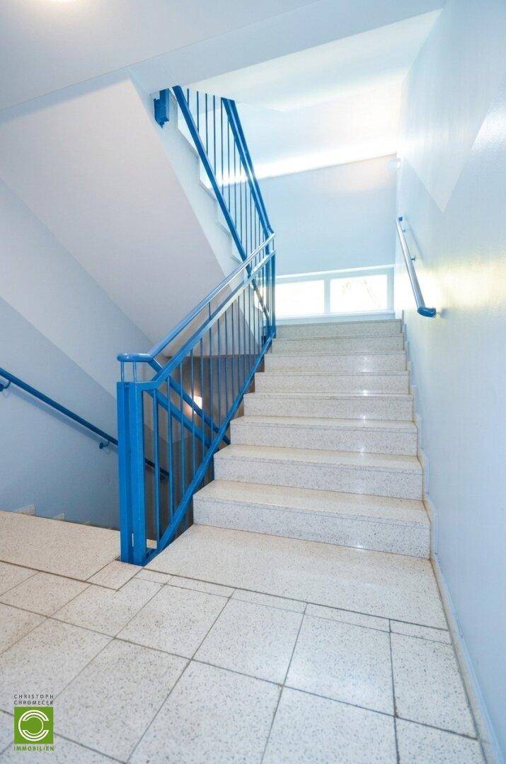 Treppenhaus mit blauen Geländern und hellen Stufen, das die Stockwerke verbindet.