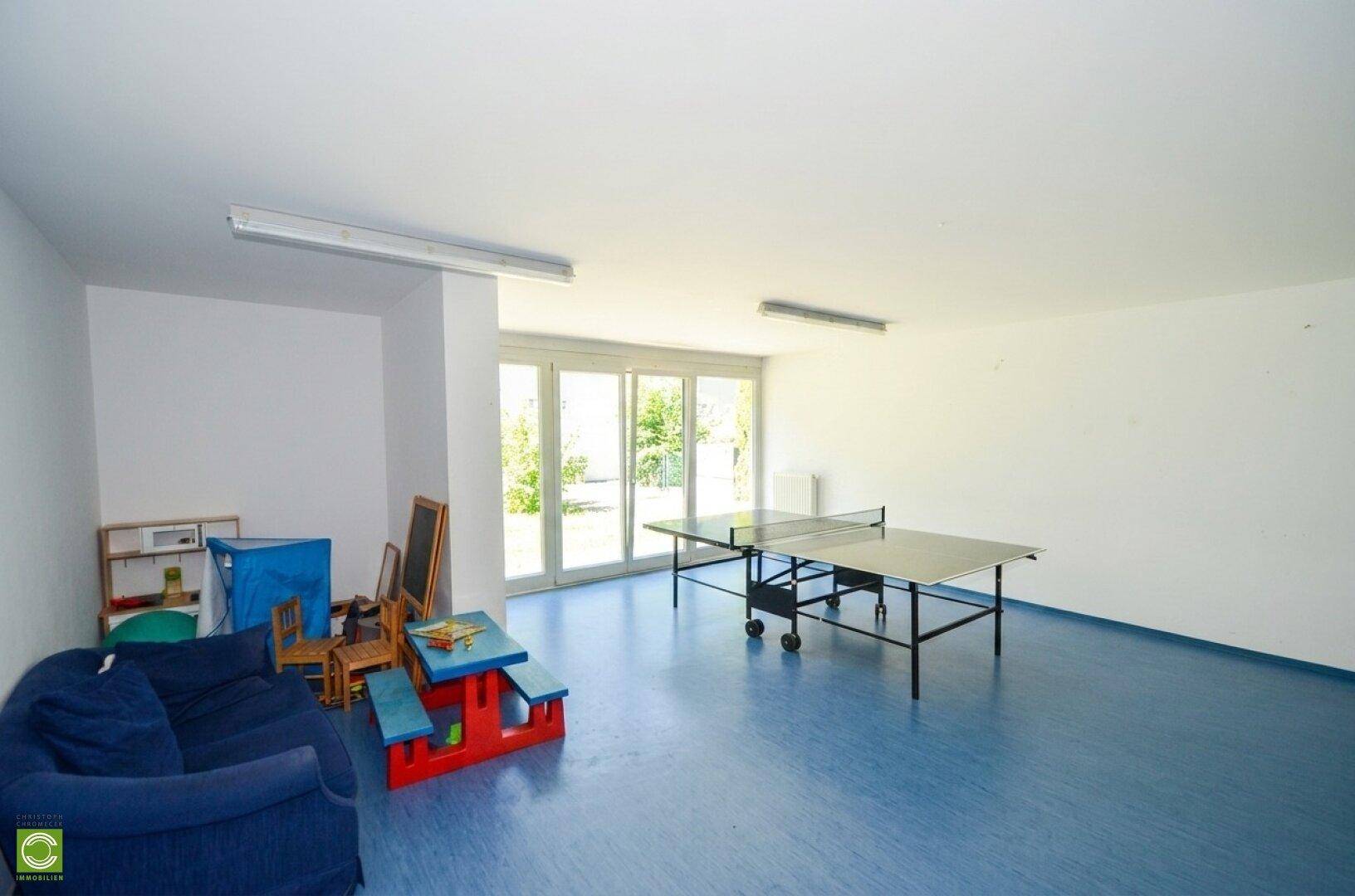 Gemeinschaftsraum mit Tischtennisplatte, Kindermöbeln und Zugang zum grünen Außenbereich.