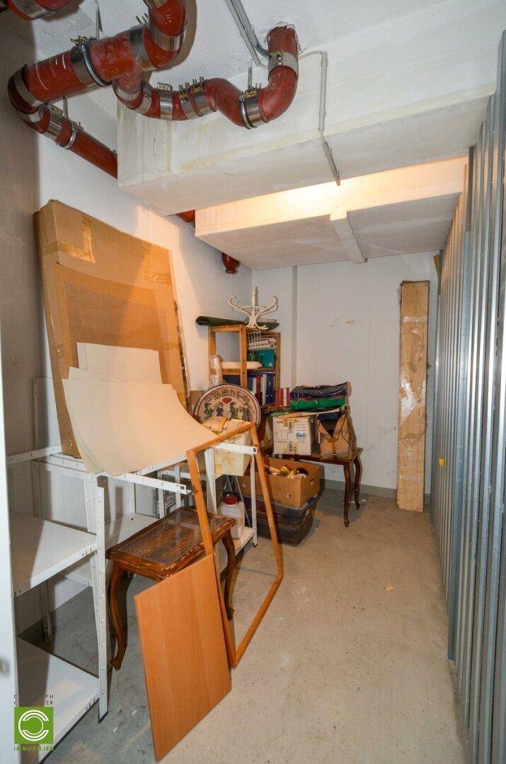 Kellerraum mit sichtbaren Rohren, Regalen und verschiedenen gelagerten Gegenständen.