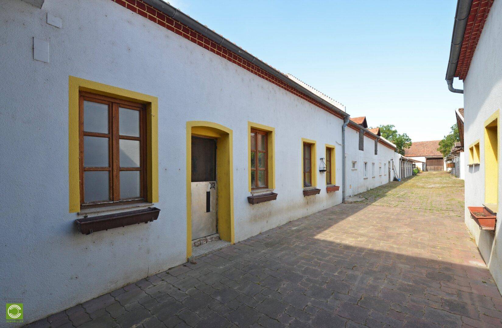 Lange Reihe weißer Gebäude mit gelben Fensterrahmen und einem gepflasterten Weg unter blauem Himmel.