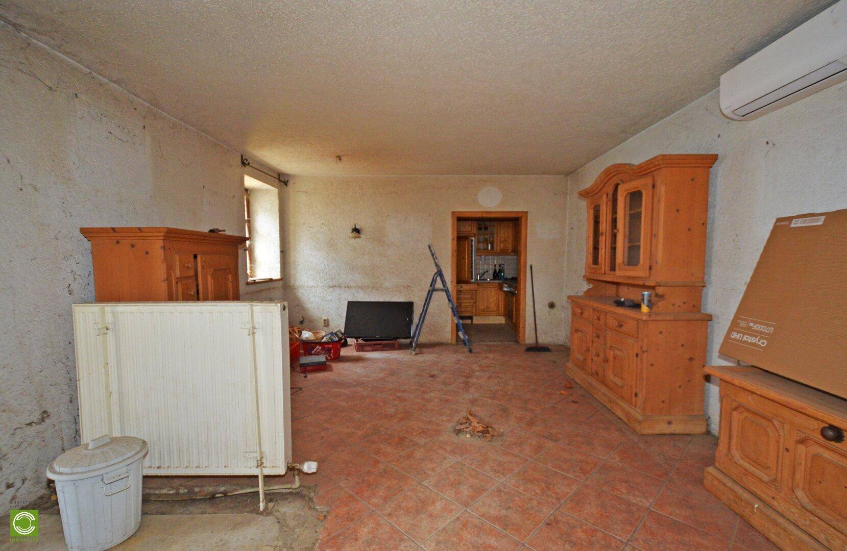 Raum mit Terrakottafliesen, Holzmöbeln und einer Klimaanlage, die auf Renovierung wartet.