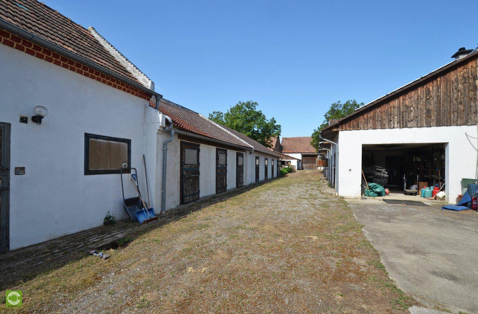 Außenbereich mit langen Gebäuden, einer Garage und einem Schotterweg unter blauem Himmel.