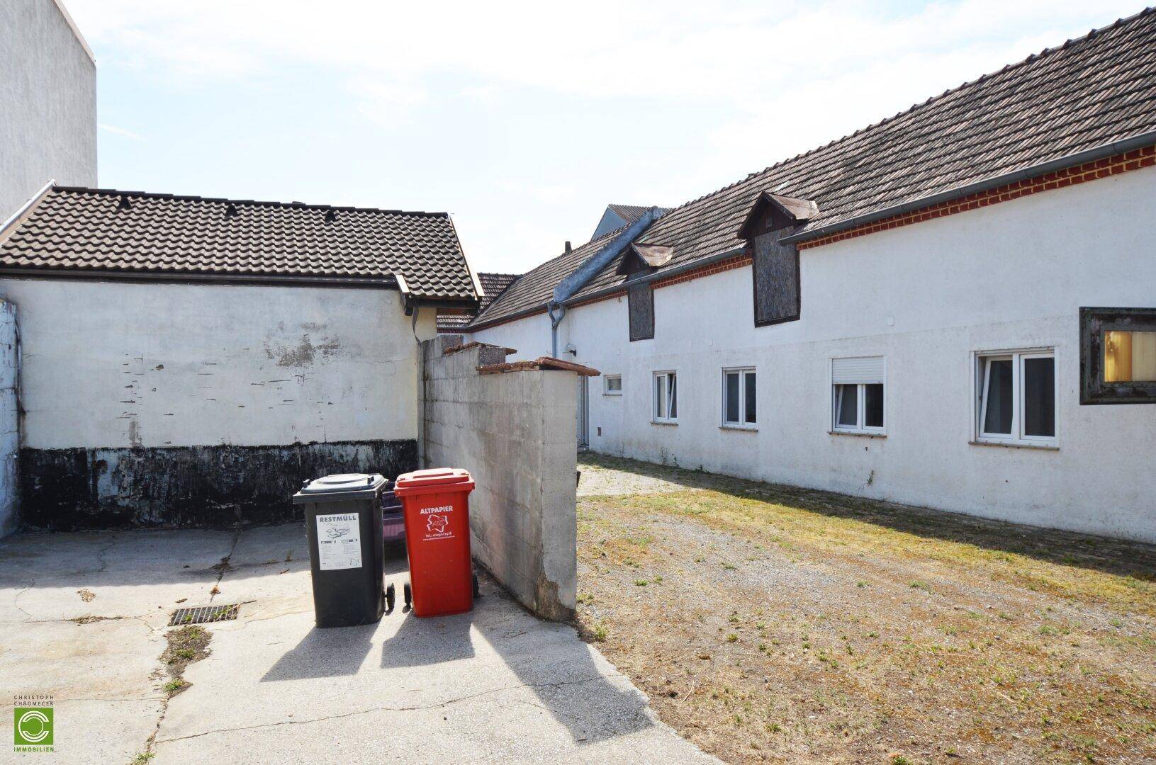 Außenbereich mit Gebäuden, einer Betonmauer und Mülltonnen, die auf Abholung warten.