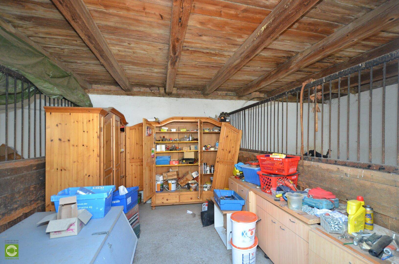 Scheuneninnenraum mit Holzbalkendecke, Metallgittern und verschiedenen Lagergegenständen.