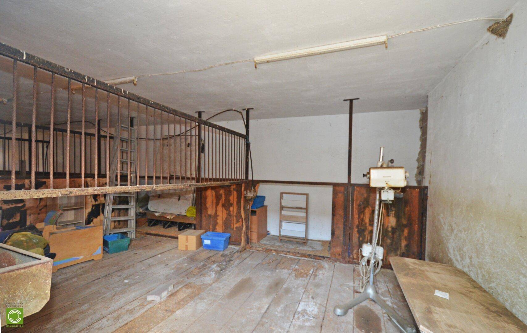 Raum mit Holzdielenboden, Metallgittern und verschiedenen Geräten, möglicherweise ein Stallbereich.