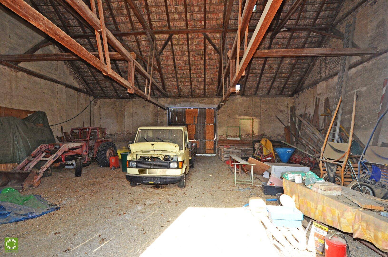 Große Scheune mit hoher Holzkonstruktion, einem Oldtimer und landwirtschaftlichen Geräten.