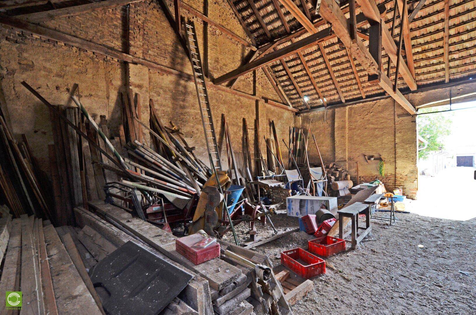 Rustikale Scheune mit Erdboden, Holzbalken und einer Ansammlung von Holzbrettern und Werkzeugen.