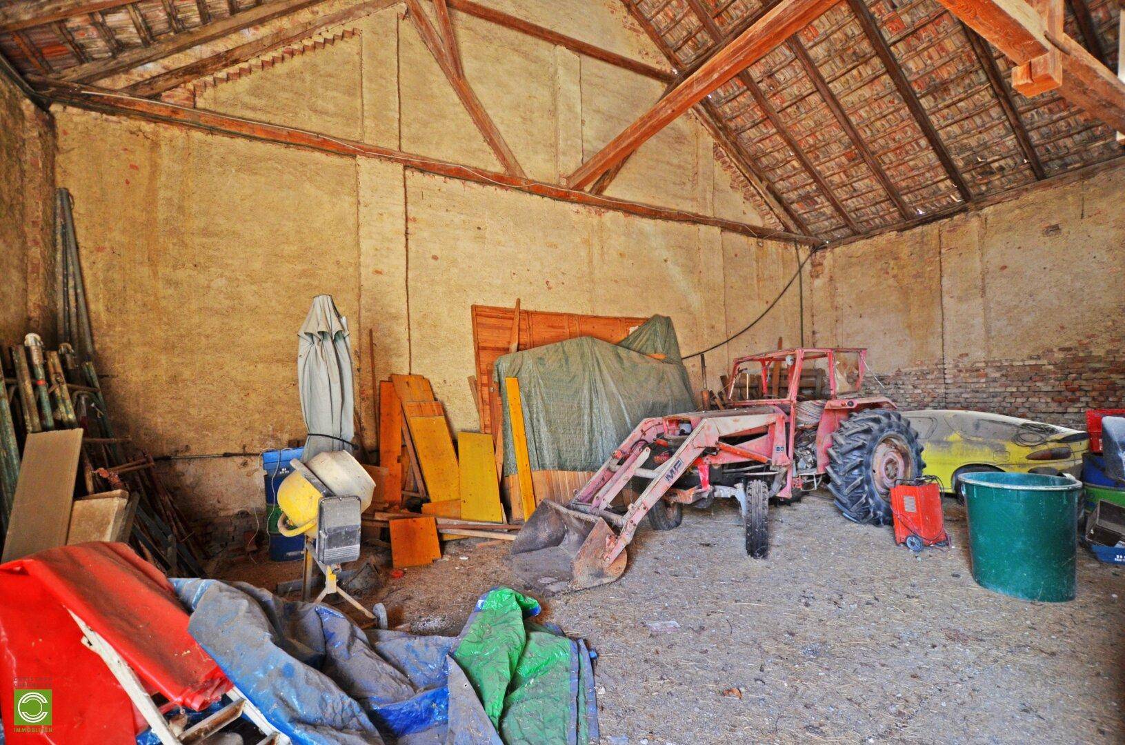Innenansicht einer Scheune mit einem roten Traktor und verschiedenen landwirtschaftlichen Geräten.