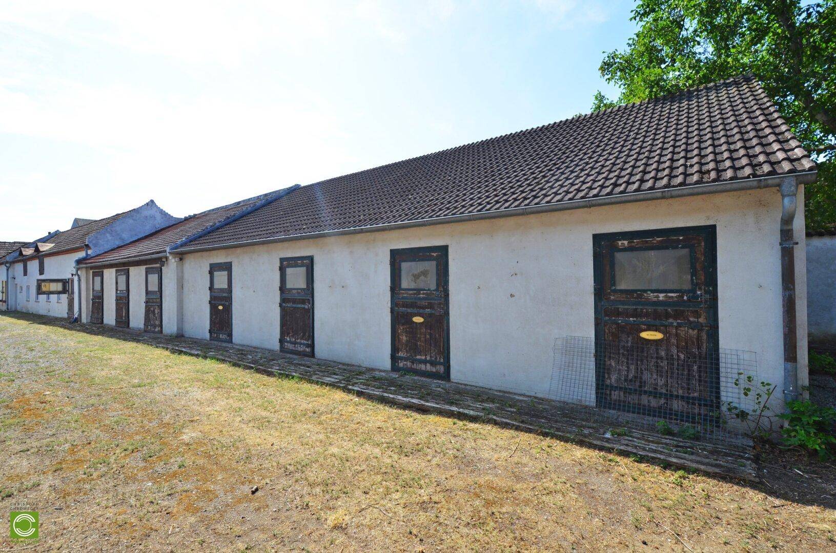 Seitenansicht des langen, weiß gestrichenen Gebäudes mit dunklen Holztüren und einem traditionellen Ziegeldach.