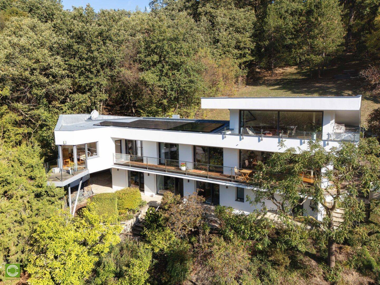 Elegantes modernes Haus in Hanglage, umgeben von Wald und mit mehreren Balkonen.