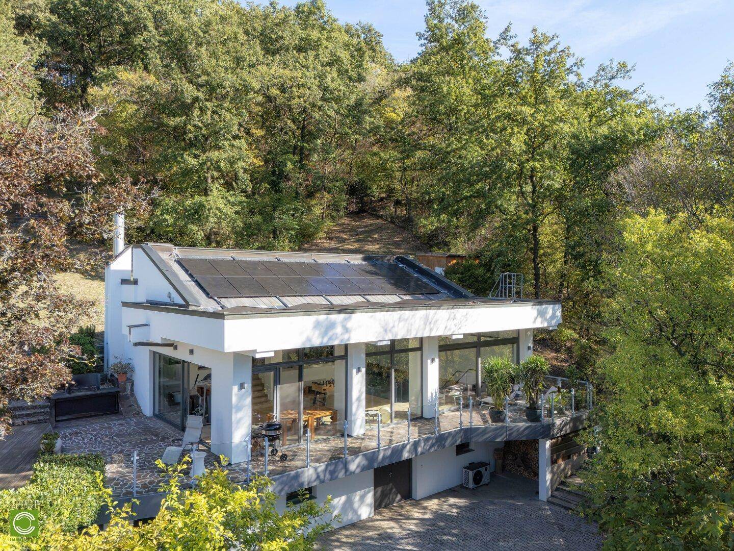 Architektonisch ansprechendes Haus mit Flachdach, Photovoltaikanlage und umliegender Natur.