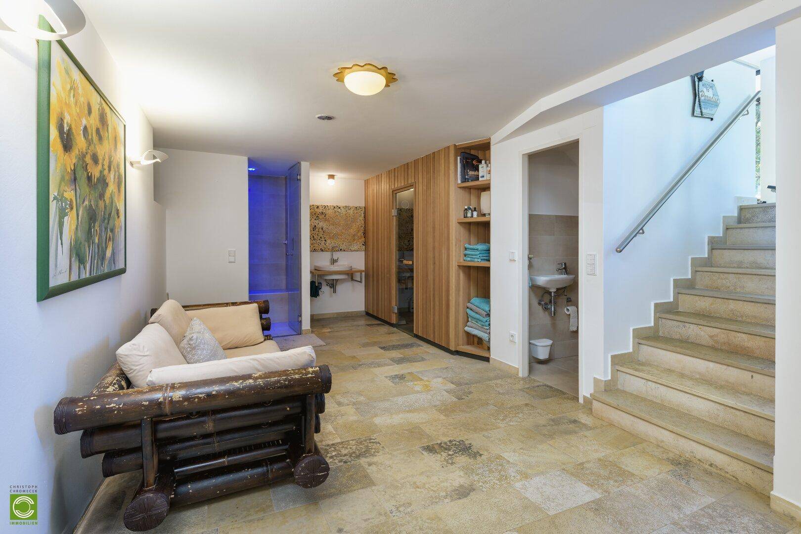 Wellnessbereich mit Entspannungsecke, Dusche und Zugang zur Sauna, ausgestattet mit Steinboden.