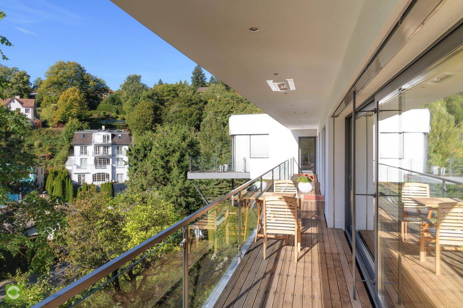 Heller Balkon mit Holzbelag und Glasgeländer, möbliert für entspannte Stunden im Freien.