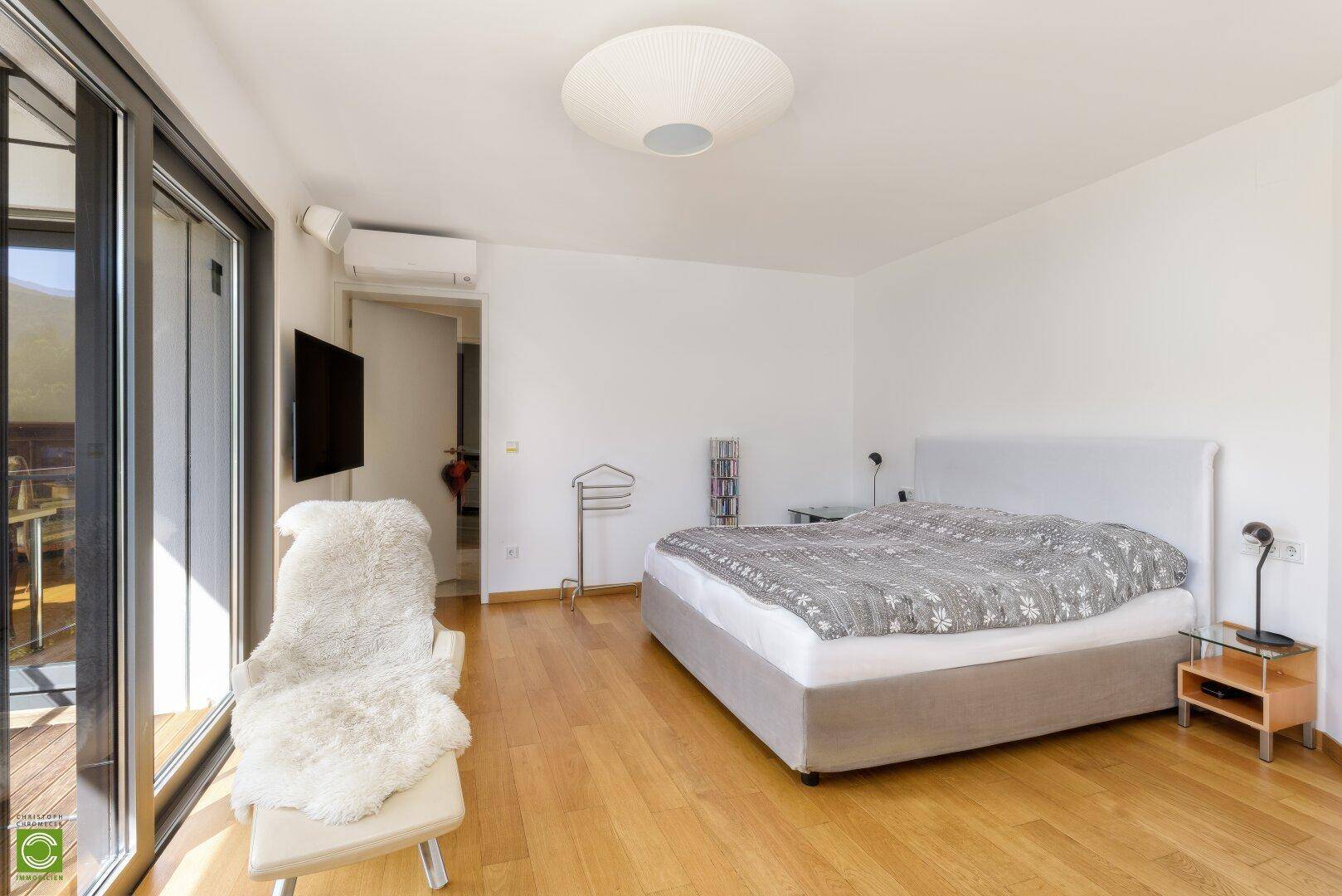 Modernes Schlafzimmer mit Holzboden, Klimaanlage und Zugang zu einem Balkon.