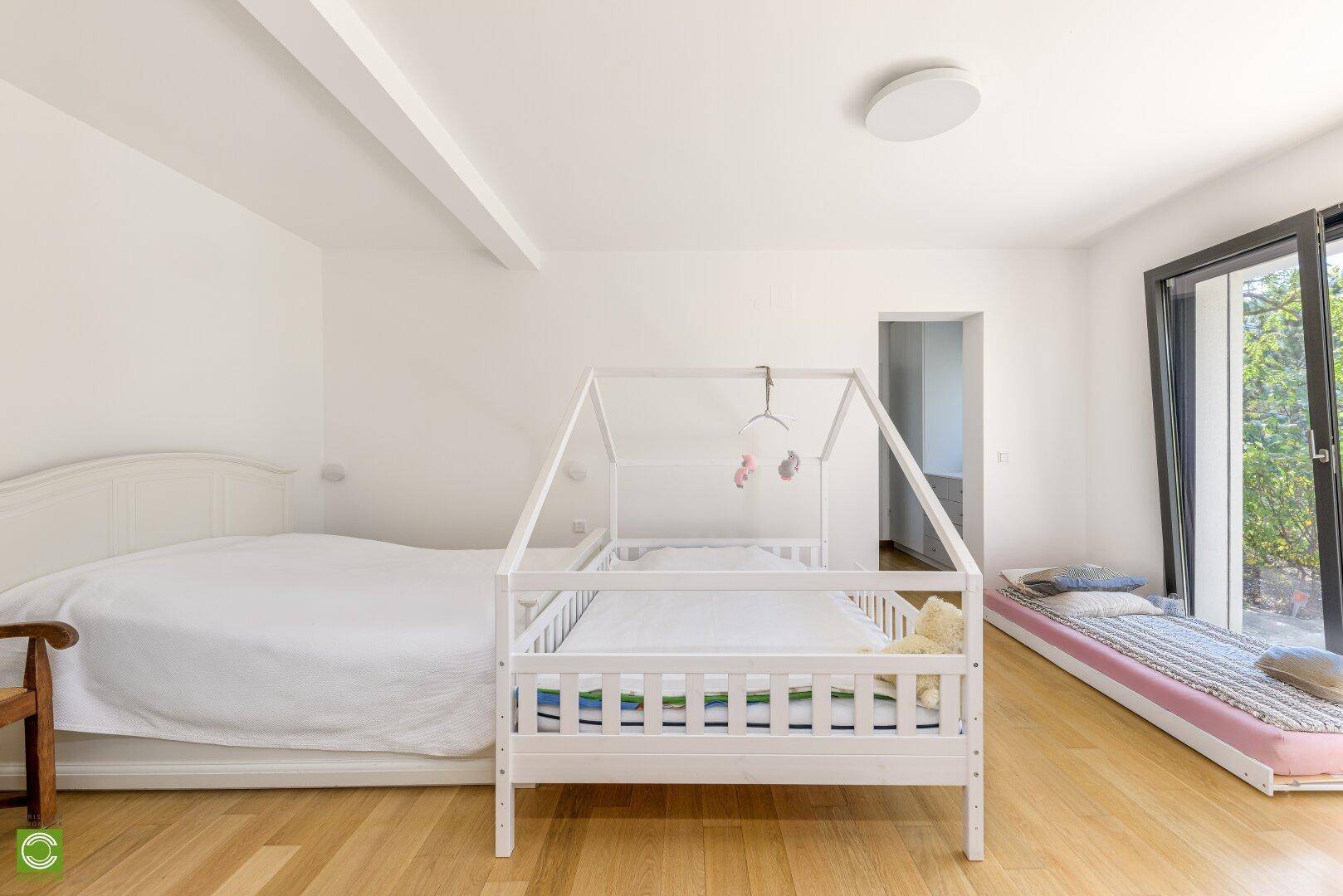 Schlafzimmer mit Holzboden, Doppelbett und Babybett, hell und freundlich gestaltet.