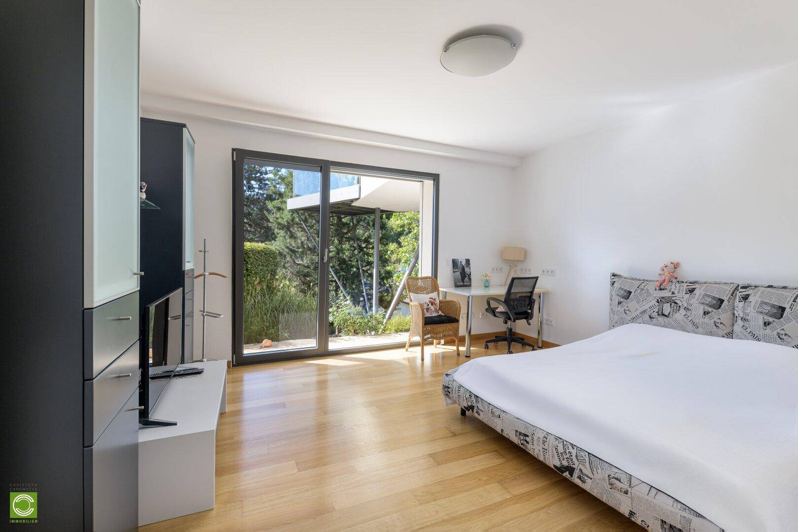 Geräumiges Schlafzimmer mit Holzboden, Schreibtisch und Zugang zur Terrasse.