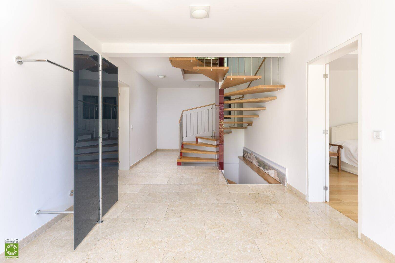 Flur mit hellem Steinboden und einer eleganten Holz-Wendeltreppe, die die Etagen verbindet.