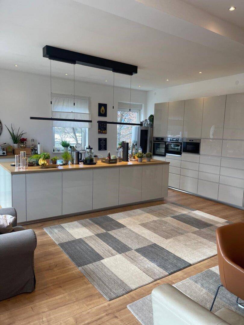 Helle, moderne Küche mit großer Kochinsel, glänzenden Schränken und Holzboden.