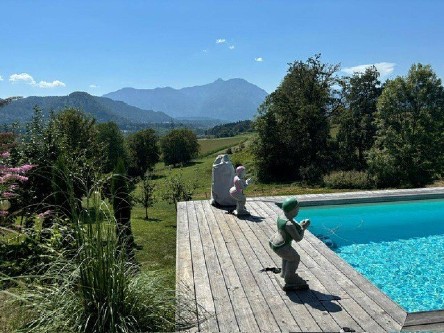 Außenpoolbereich mit Holzdeck, dekorativen Figuren und weitem Blick auf die Berge.