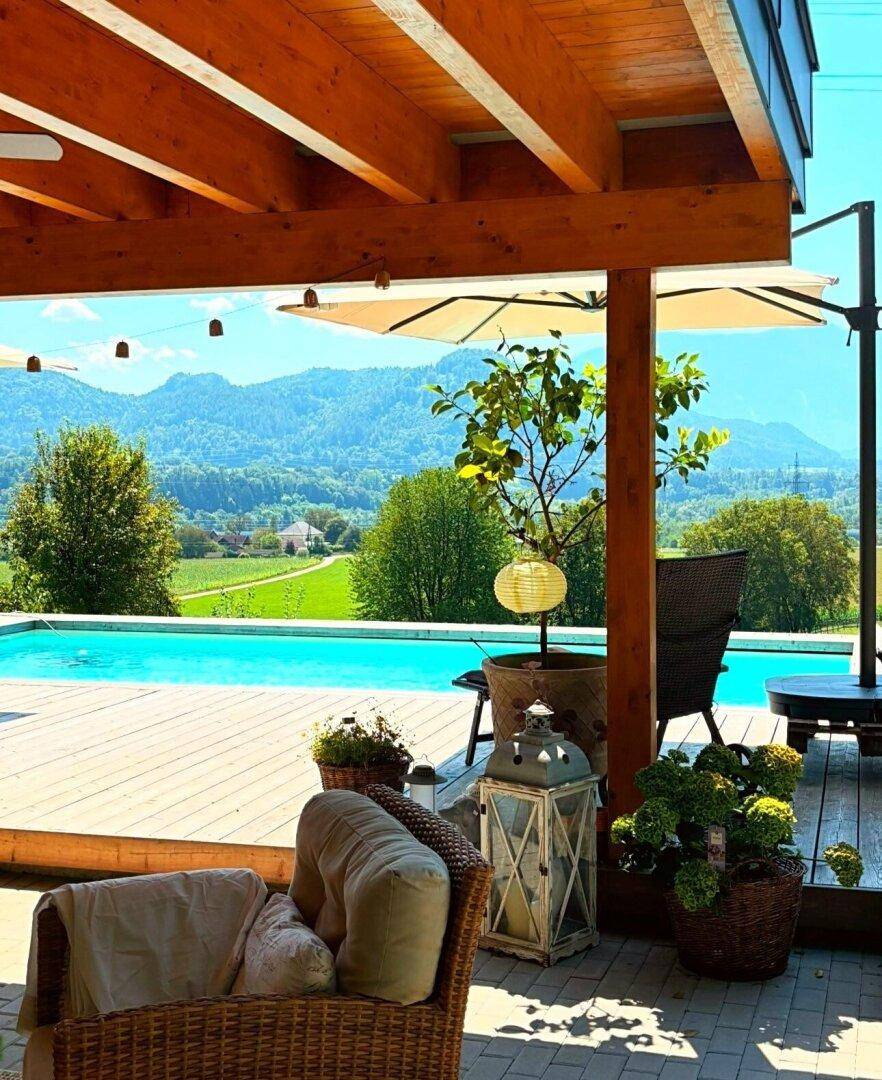 Gemütlicher überdachter Terrassenbereich mit Lounge-Möbeln, Pflanzen und Blick auf den Pool und die Berge.