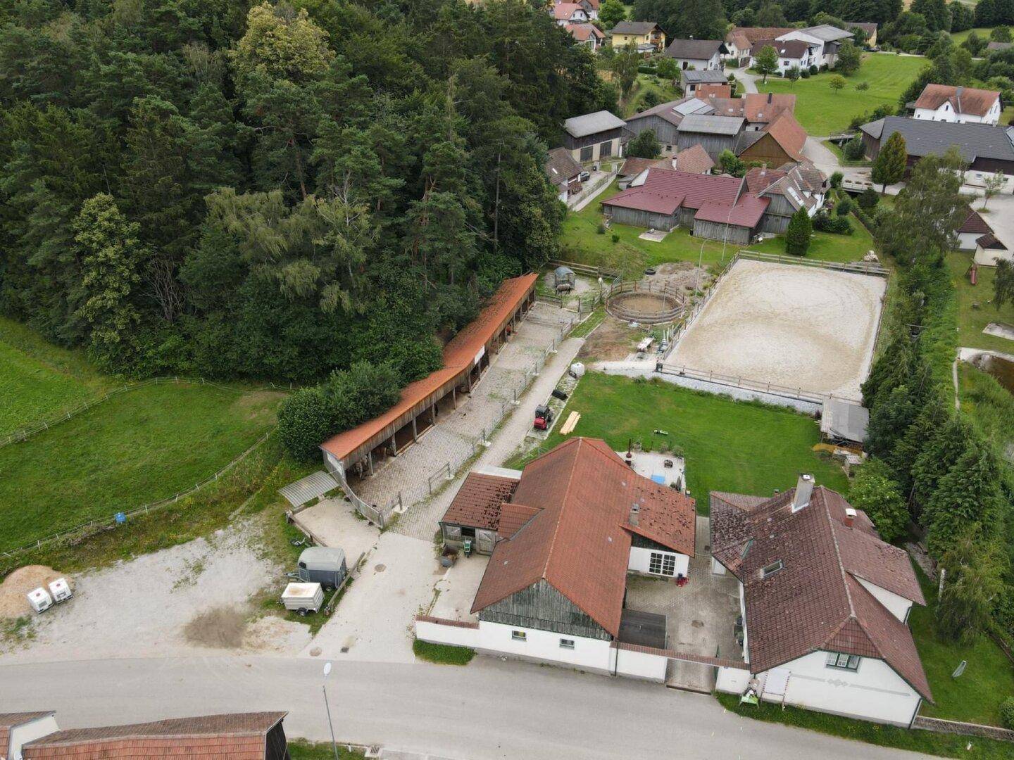 Luftaufnahme eines Anwesens mit Wohnhaus, Stallungen, Reitplatz und angrenzendem Wald.